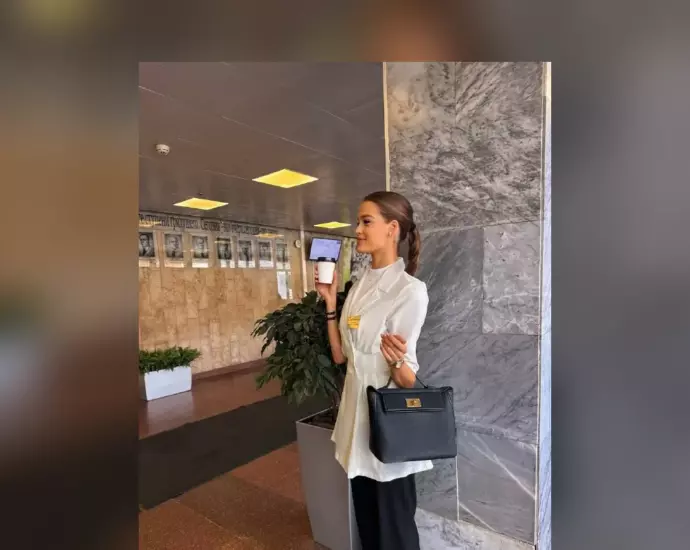 Валентина Алексеева в белом костюме с кофе и сумкой в холле