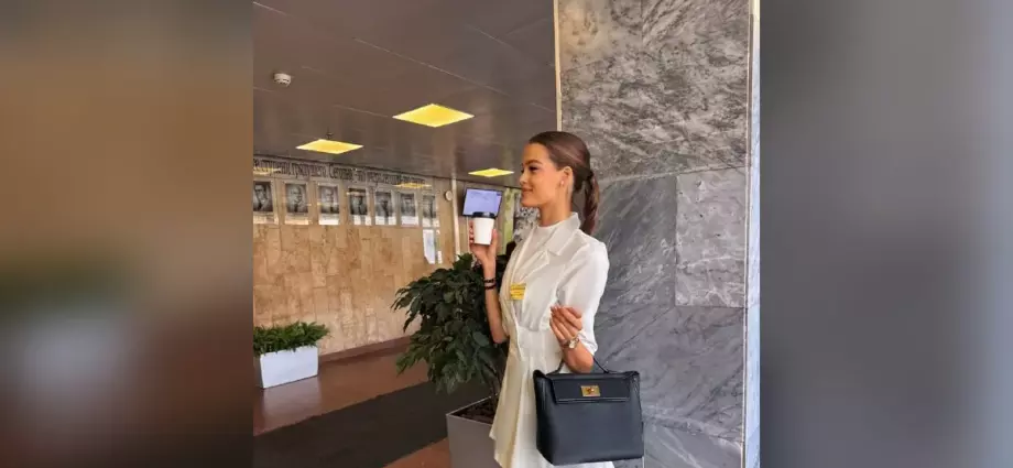 Валентина Алексеева в белом костюме с кофе и сумкой в холле