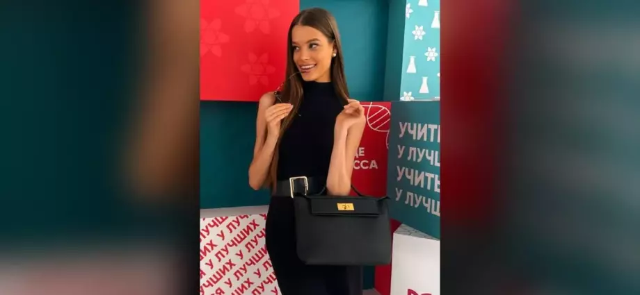 Валентина Алексеева в чёрном платье с сумкой позирует у ярких стендов